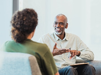 A man and woman sitting in chairs facing each other and talking
